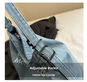 Detail of adjustable black buckle and white text on blue denim tote bag with zipper