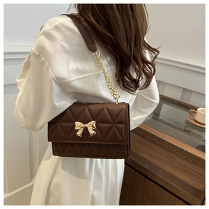 Detail of a dark brown crossbody bag with diamond quilting and gold bow metal buckle