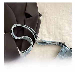 Detail view of adjustable denim shoulder strap and stitching on blue crossbody tote bag