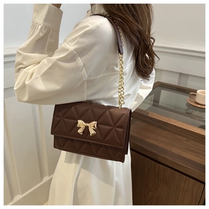 Detail of dark brown quilted shoulder bag with golden bow clasp and chain strap