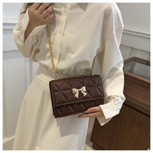 Detailed close-up of dark brown quilted crossbody bag featuring a golden bow buckle