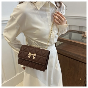 Detail of dark brown quilted shoulder bag with golden bow clasp and chain strap