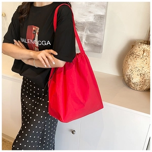 Detail of red nylon bucket bag with drawstring closure worn by a model in interior