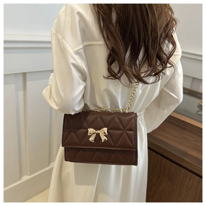 Detail showing brown quilted PU leather crossbody bag with golden bow and chain strap