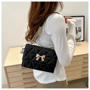Detail of black quilted shoulder bag featuring gold bow hardware and chain strap