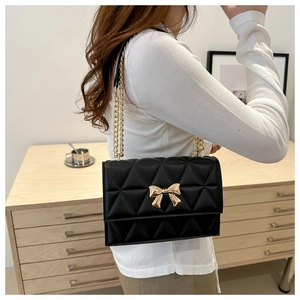 Close-up of black quilted shoulder bag with golden bow clasp and metal chain strap