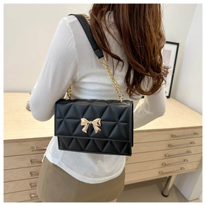 Detail of black quilted shoulder bag featuring gold bow hardware and chain strap
