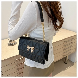 Detail of black quilted crossbody bag featuring a golden bow buckle and chain strap