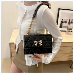 Detail of black quilted shoulder bag with gold bow clasp and metal chain on a model