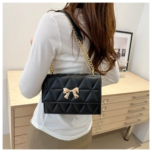 Detail shot of a black quilted crossbody bag with a gold metal bow on a shoulder chain