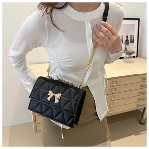 Detail of black quilted bag with golden bow buckle and chain strap on a model