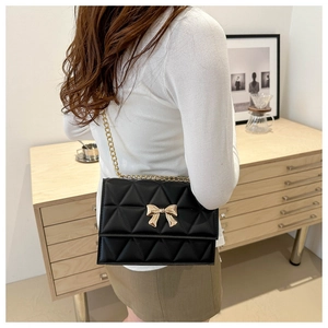 Detailed view of black quilted crossbody bag with gold bow clasp on a female model