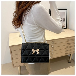 Detail of black quilted shoulder bag with golden bow clasp shown on a model