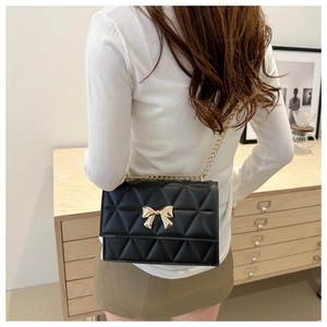 Close-up of quilted chain bag featuring a decorative gold bow buckle and metal strap