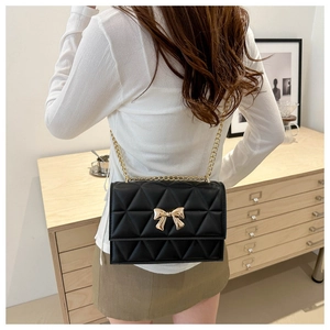 Rear view of a model wearing a black quilted crossbody bag with a gold bow clasp and chain