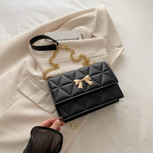 Elegant black quilted crossbody bag with golden bow clasp and metal chain strap