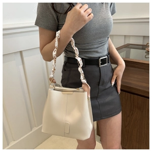 Detail of a beige bucket bag with an elegant silk scarf wrapped around the chain strap