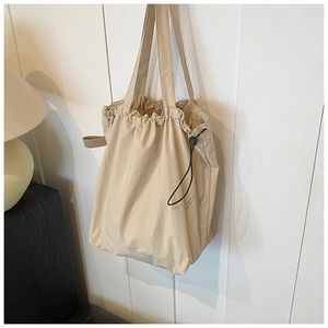 Detailed close-up of beige nylon bucket bag drawstring and cord lock on wall