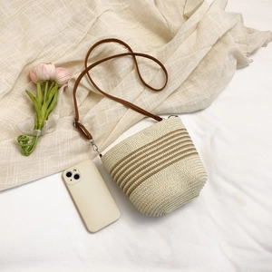Top-down view of a woven bucket bag with brown leather strap on soft linen fabric