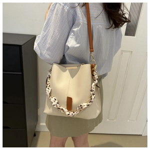 Detail of beige bucket bag featuring leopard print silk scarf wrapped on metal chain handle