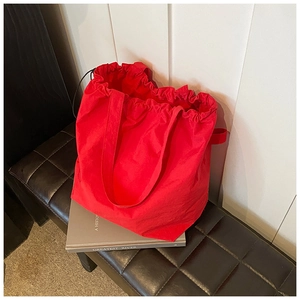 Detail showing bright red nylon drawstring bucket bag with pleated ruffles on a leather stool