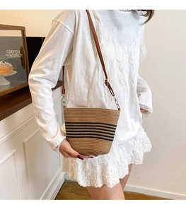 Detail shot of woven bucket bag featuring black stripes and brown leather strap