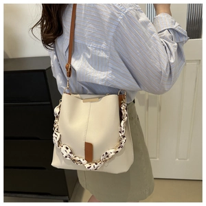 Detail of cream bucket bag with floral scarf handle and brown leather shoulder strap