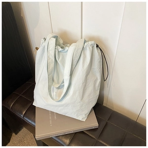 Close-up of light blue nylon bucket bag with adjustable black drawstrings on a bench