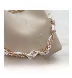 Detail of beige faux leather handbag with gold chain strap and floral silk scarf wrap