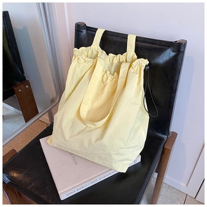 Detailed view of yellow nylon bucket bag with drawstring design on a leather chair