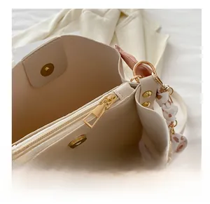 Detailed close-up of cream leather bucket bag showing gold zipper and silk scarf handle