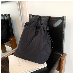 Close-up of black nylon bucket bag on chair showing smooth texture and drawstring detail