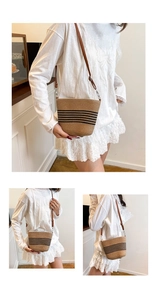 Detail of woven straw bucket bag with black stripes and brown leather strap on model