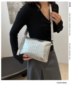 Silver envelope clutch bag with crocodile texture and fabric strap worn by a model