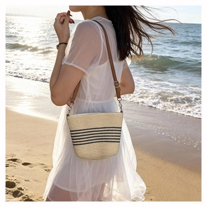 Detail of woven straw bucket bag with black stripes and brown leather shoulder strap