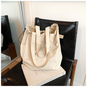 Detail of minimalist cream nylon bucket bag with ruffled drawstring closure on armchair