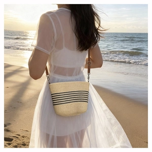 Detail of woven straw bucket bag with black stripes and leather strap on a beach