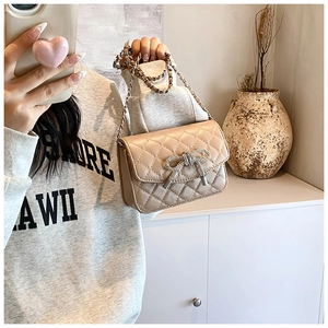 Detail van beige gewatteerde handtas met sprankelende strass-strik en zilveren ketting