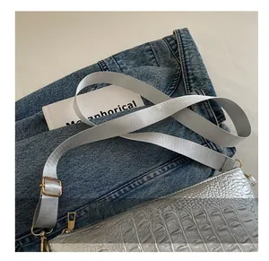 Detail of silver crocodile pattern shoulder bag with a wide adjustable fabric strap
