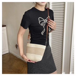Detail view of woven straw bucket bag with brown stripes and leather shoulder strap on model