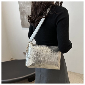 Detail of silver crocodile-embossed crossbody bag worn by model in a minimalist setting