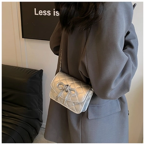 Detail van een zilveren gewatteerde crossbodytas met strass-strik en metalen ketting