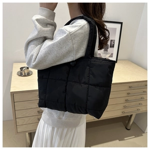 Detail of black quilted tote bag with padded square texture worn on shoulder