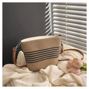 Detail of woven straw bucket bag with black stripes and brown leather strap on soft linen