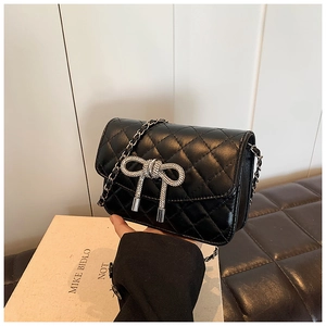 Detail van zwarte gewatteerde crossbodytas met strass-strik en metalen kettingriem