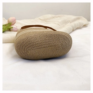 Detailed view of natural straw woven bucket bag with brown leather strap and sturdy base