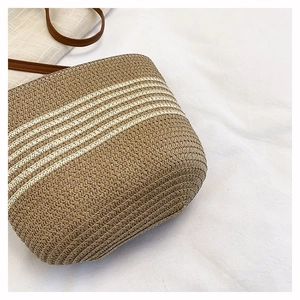 Close-up of woven bucket bag with khaki stripes and brown leather shoulder strap
