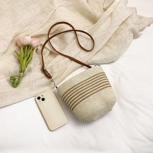 Detailed macro view of woven straw bucket bag with dark brown stripes and leather strap