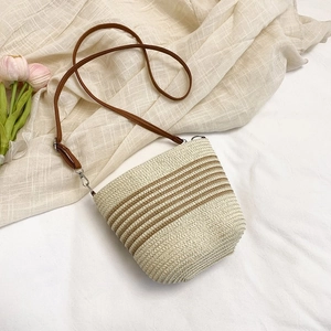 Close-up of woven straw bucket bag with brown stripes and slim leather strap