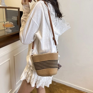 Detail of woven straw bucket bag showing khaki stripes and adjustable leather strap
